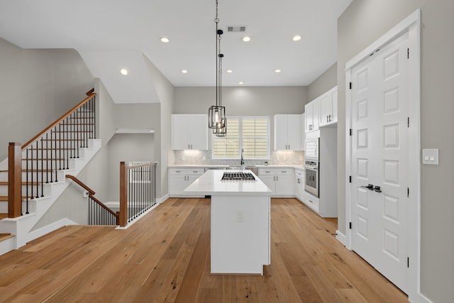 1139 W 22nd St, Houston, TX 77008 - kitchen featuring appliances with stainless steel finishes, a kitchen island, light wood finished floors, white cabinetry, and tasteful backsplash