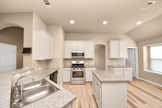 7315 Palmito Ranch Dr, Richmond, TX 77406 - kitchen featuring appliances with stainless steel finishes, arched walkways, a sink, light wood-style flooring, and white cabinetry