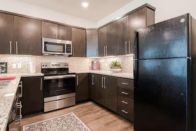 442 William D Fitch, College Station, TX 77845 - kitchen with stainless steel appliances, dark brown cabinets, light wood-style floors, tasteful backsplash, and light stone counters