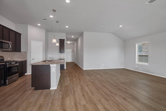 2314 Brickfielder Ln, Baytown, TX 77523 - kitchen featuring appliances with stainless steel finishes, light stone countertops, light wood finished floors, dark brown cabinetry, and a kitchen island with sink