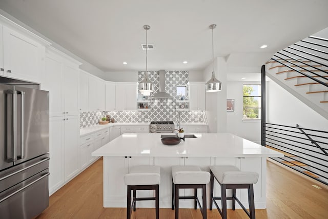 828 Wakefield Dr Unit B, Houston, TX 77018 - kitchen featuring appliances with stainless steel finishes, wall chimney exhaust hood, decorative backsplash, light wood-style flooring, and a kitchen bar