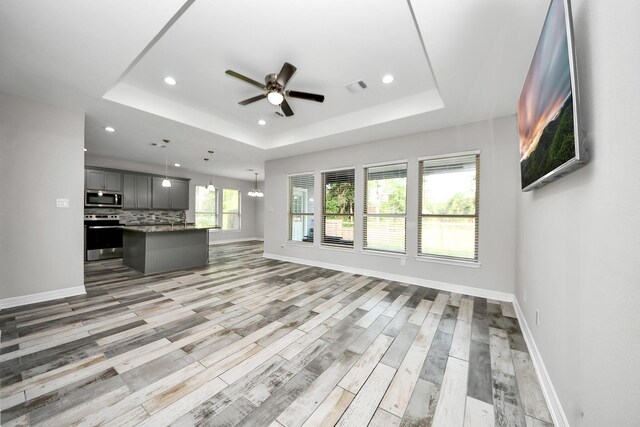 25450 Killarney St, Hempstead, TX 77445 - unfurnished living room featuring a tray ceiling, a ceiling fan, recessed lighting, light wood-style flooring, and baseboards