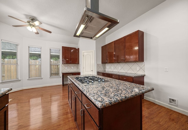 1803 Mustang Xing, Missouri City, TX 77459 - kitchen with stainless steel gas stovetop, wall chimney range hood, a ceiling fan, wood finished floors, and backsplash