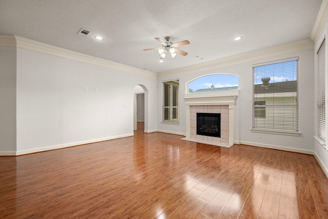 1803 Mustang Xing, Missouri City, TX 77459 - unfurnished living room with a ceiling fan, ornamental molding, arched walkways, wood finished floors, and a tile fireplace
