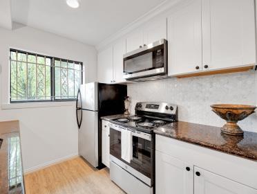 3809 N Braeswood Unit 14, Houston, TX 77025 - kitchen with stainless steel appliances, backsplash, white cabinets, light wood-type flooring, and baseboards