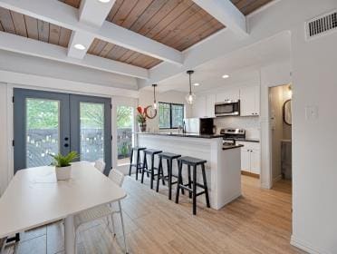 3809 N Braeswood Unit 14, Houston, TX 77025 - kitchen featuring appliances with stainless steel finishes, white cabinetry, a kitchen bar, wood ceiling with exposed beams, and light wood-style floors