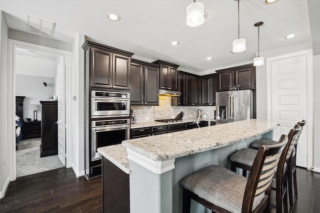 12226 Brighton Brook Ln, Tomball, TX 77377 - kitchen with appliances with stainless steel finishes, under cabinet range hood, baseboards, dark brown cabinetry, and pendant lighting