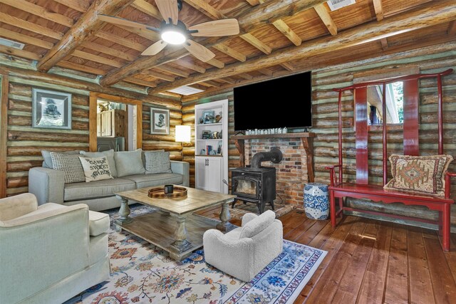 1356 Pegoda Ranch Rd, Woodlake, TX 75865 - living room featuring rustic walls, a wood stove, wooden ceiling with exposed beams, hardwood / wood-style flooring, and ceiling fan