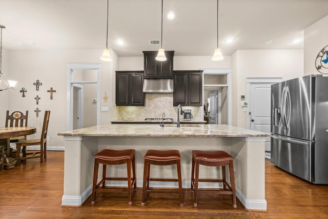 143 Jacks Corner Dr, Montgomery, TX 77316 - kitchen with stainless steel fridge, under cabinet range hood, decorative backsplash, a breakfast bar area, and a kitchen island with sink