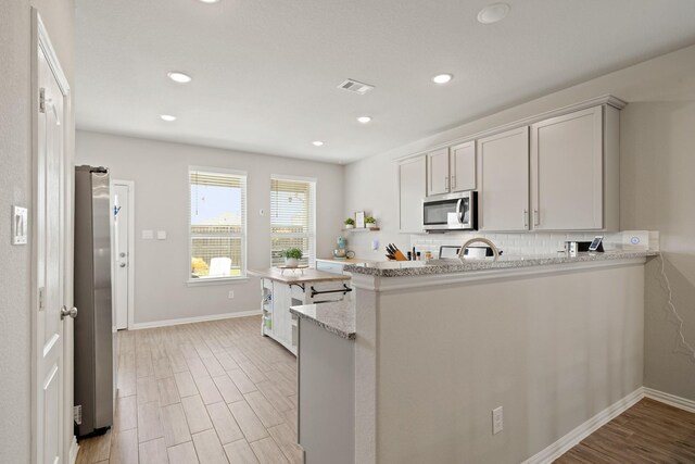 7410 Arabian Moon Trl, Fulshear, TX 77441 - kitchen featuring appliances with stainless steel finishes, decorative backsplash, baseboards, a peninsula, and light wood-style floors