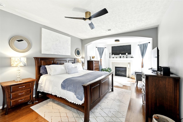 8210 Edenwood Dr, Spring, TX 77389 - bedroom with light wood-style flooring, a glass covered fireplace, a ceiling fan, and a textured ceiling
