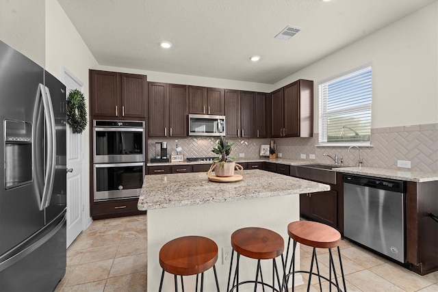 25419 Whitehaven Gate St, Katy, TX 77493 - kitchen with stainless steel appliances, a sink, dark brown cabinets, decorative backsplash, and a center island