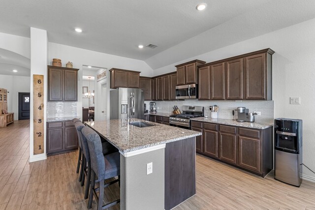 15010 Lake Shore Ave, Mont Belvieu, TX 77523 - kitchen with stainless steel appliances, a sink, dark brown cabinets, decorative backsplash, and lofted ceiling