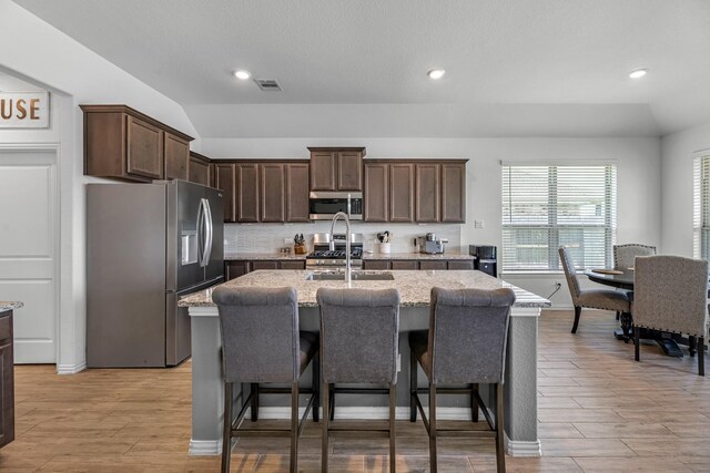 15010 Lake Shore Ave, Mont Belvieu, TX 77523 - kitchen with stainless steel appliances, a sink, dark brown cabinets, light stone counters, and a kitchen island with sink