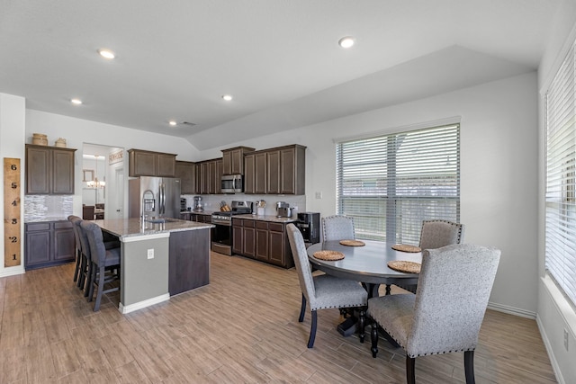 15010 Lake Shore Ave, Mont Belvieu, TX 77523 - kitchen with stainless steel appliances, a center island with sink, vaulted ceiling, healthy amount of natural light, and dark brown cabinets