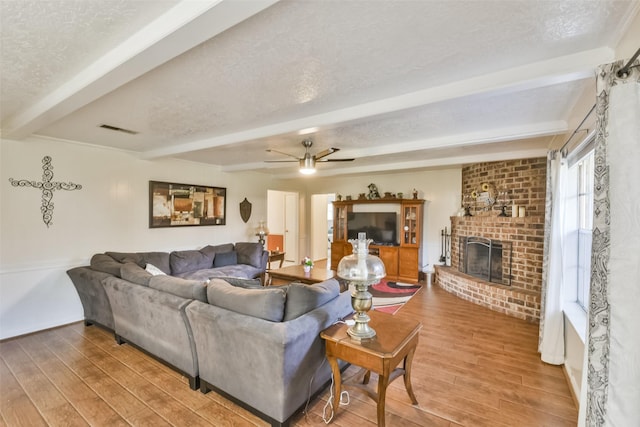 1805 Twila Ln, Conroe, TX 77301 - living room with beam ceiling, wood finished floors, a brick fireplace, a textured ceiling, and a ceiling fan