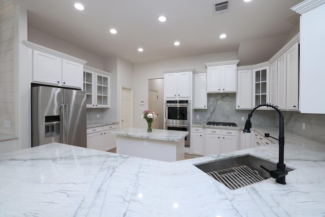6 Lovenote Ct, The Woodlands, TX 77382 - kitchen featuring appliances with stainless steel finishes, a sink, backsplash, light stone countertops, and white cabinetry