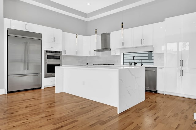 1505 Stuart St, Houston, TX 77004 - kitchen featuring appliances with stainless steel finishes, wall chimney range hood, light countertops, light wood-style floors, and a towering ceiling