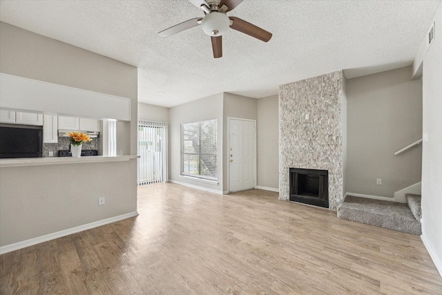 3754 Tanglewilde St N Unit C3, Houston, TX 77063 - unfurnished living room with light wood-style flooring, a ceiling fan, a large fireplace, a textured ceiling, and stairs