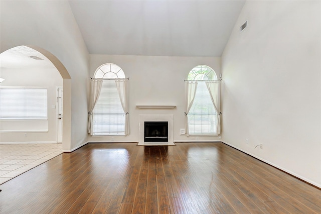 17935 Western Pass Ln, Houston, TX 77095 - unfurnished living room featuring high vaulted ceiling, a fireplace with flush hearth, baseboards, wood finished floors, and arched walkways