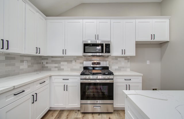 4506 Knights Ct, Baytown, TX 77521 - kitchen with stainless steel appliances, vaulted ceiling, white cabinetry, light wood-style floors, and backsplash
