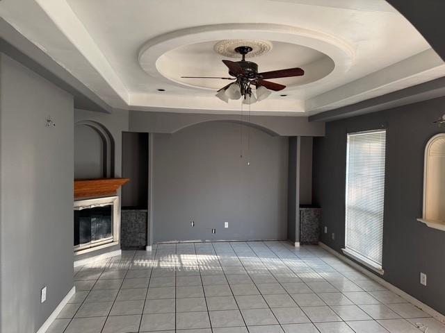 13023 High Star Dr, Houston, TX 77072 - unfurnished living room with a tray ceiling, a ceiling fan, light tile patterned flooring, and a glass covered fireplace