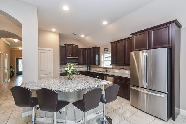 19527 Sundance Edge Ct, Richmond, TX 77407 - kitchen featuring appliances with stainless steel finishes, arched walkways, decorative backsplash, light stone counters, and a center island