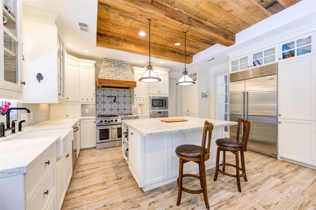 62 W Mirror Ridge Cir, The Woodlands, TX 77382 - kitchen with built in appliances, wooden ceiling, wall chimney range hood, a sink, and a center island