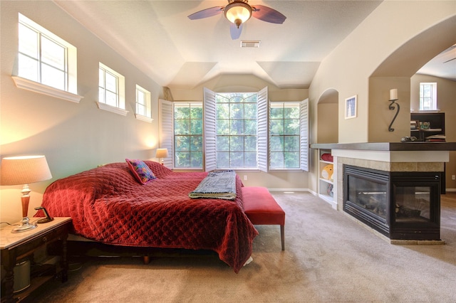 62 W Mirror Ridge Cir, The Woodlands, TX 77382 - carpeted bedroom featuring a tiled fireplace, baseboards, lofted ceiling, ceiling fan, and arched walkways