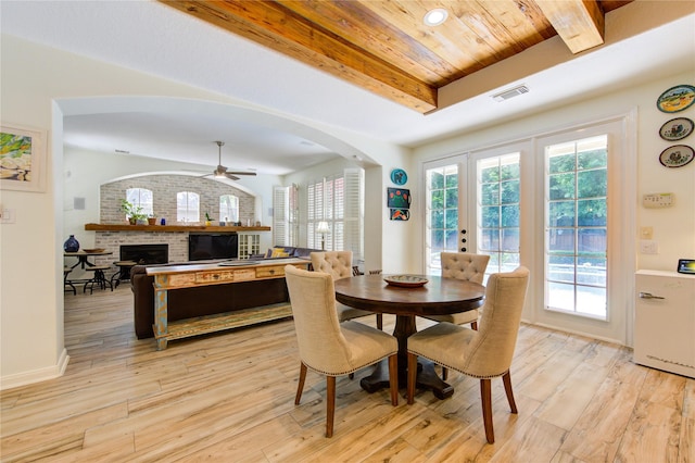 62 W Mirror Ridge Cir, The Woodlands, TX 77382 - dining space featuring a brick fireplace, ceiling fan, plenty of natural light, light wood-type flooring, and wood ceiling with exposed beams