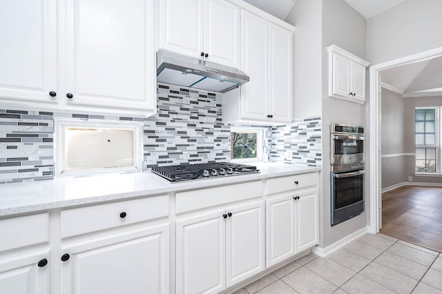 2604 Sunday House Ct, Pearland, TX 77584 - kitchen with under cabinet range hood, white cabinetry, light tile patterned floors, and decorative backsplash