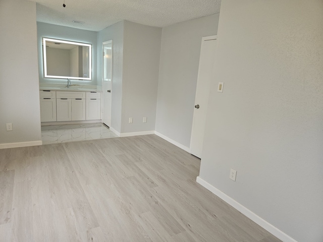 21631 Park Villa Dr, Katy, TX 77450 - empty room featuring a textured ceiling, light wood-style floors, baseboards, and a sink