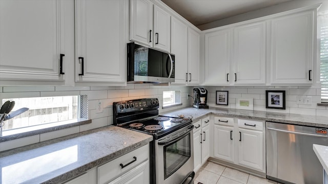 20703 Emerald Spruce Ct, Kingwood, TX 77346 - kitchen with stainless steel appliances, white cabinetry, backsplash, light tile patterned floors, and light stone countertops