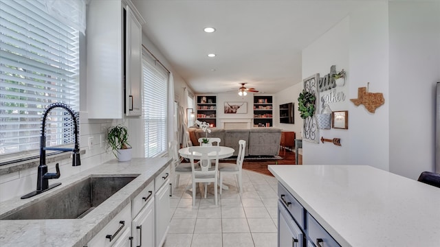 20703 Emerald Spruce Ct, Kingwood, TX 77346 - kitchen with a sink, ceiling fan, a fireplace, light stone counters, and white cabinetry