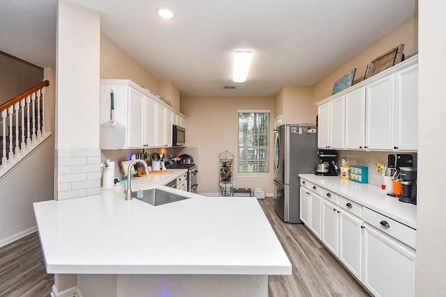 2206 Rocky Hollow Ln, Katy, TX 77450 - kitchen featuring stainless steel appliances, a sink, light wood finished floors, tasteful backsplash, and white cabinets