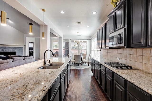 8106 Yarrow Dr, Cypress, TX 77433 - kitchen featuring a sink, stainless steel appliances, dark cabinets, a stone fireplace, and healthy amount of natural light