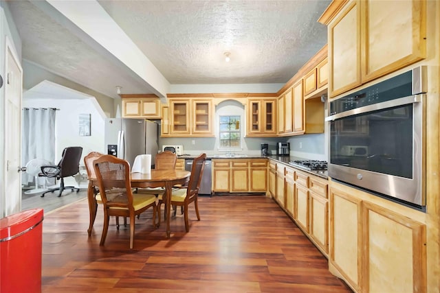 1206 Dewalt St, Houston, TX 77088 - kitchen with stainless steel appliances, light brown cabinetry, a textured ceiling, dark wood-type flooring, and glass insert cabinets