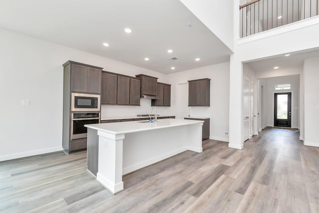 21118 Chelton Beach Dr, Cypress, TX 77433 - kitchen featuring stainless steel oven, a center island with sink, built in microwave, light wood finished floors, and recessed lighting