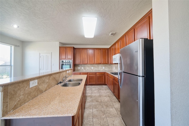 6610 Autumn Sunset Ln, Spring, TX 77379 - kitchen featuring stainless steel appliances, a sink, decorative backsplash, brown cabinetry, and a textured ceiling