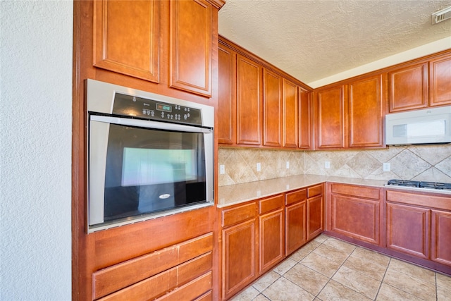 6610 Autumn Sunset Ln, Spring, TX 77379 - kitchen featuring stainless steel appliances, light countertops, backsplash, a textured ceiling, and light tile patterned floors