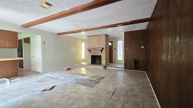 3823 Regency Dr, Houston, TX 77045 - unfurnished living room with beam ceiling, a brick fireplace, a textured ceiling, and wood walls