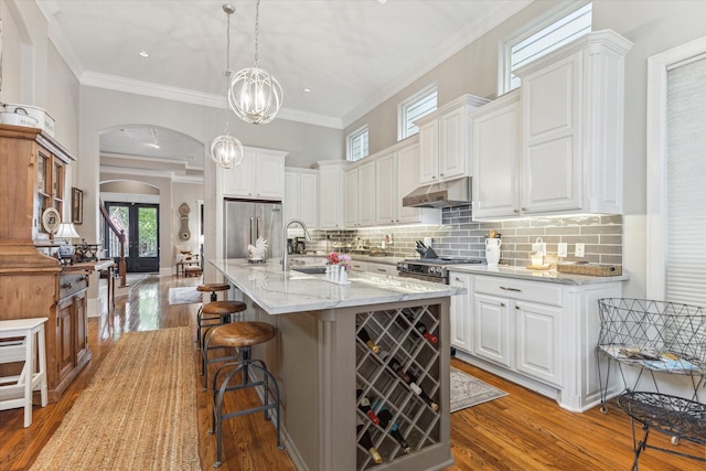 414 E 28th St, Houston, TX 77008 - kitchen featuring high quality appliances, arched walkways, under cabinet range hood, light wood-style flooring, and crown molding