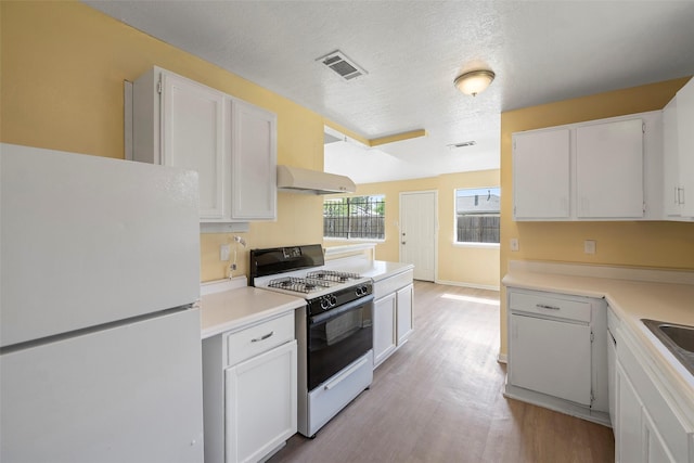 14118 Magnolia Springs Dr, Houston, TX 77066 - kitchen featuring freestanding refrigerator, range with gas stovetop, under cabinet range hood, light wood-style flooring, and white cabinetry