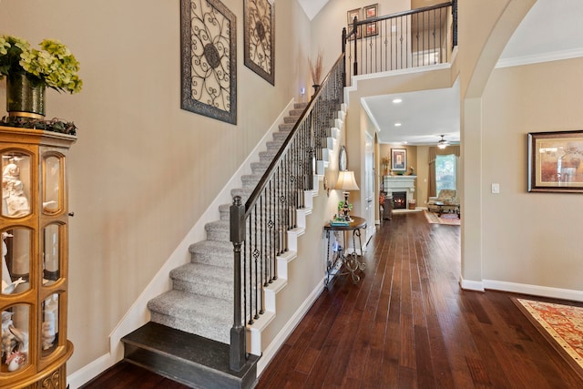 24119 Blue Crest Dr, Porter, TX 77365 - staircase with wood-type flooring, a ceiling fan, baseboards, a lit fireplace, and a towering ceiling