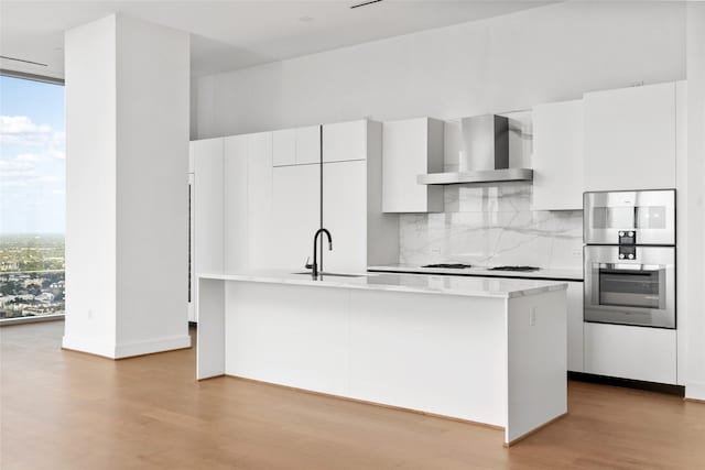 1711 Allen Pkwy Unit 3401, Houston, TX 77019 - kitchen featuring wall chimney exhaust hood, a sink, wood finished floors, decorative backsplash, and light countertops