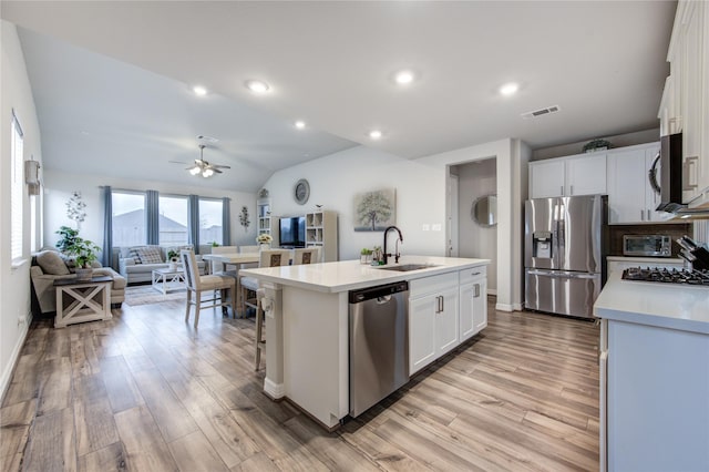 2432 Solaris Bend Dr, Katy, TX 77493 - kitchen with stainless steel appliances, a sink, light wood finished floors, an island with sink, and vaulted ceiling
