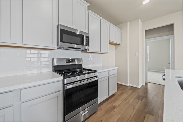 27506 Beachside Arbor Dr, Katy, TX 77493 - kitchen featuring appliances with stainless steel finishes, light wood-type flooring, tasteful backsplash, white cabinets, and baseboards