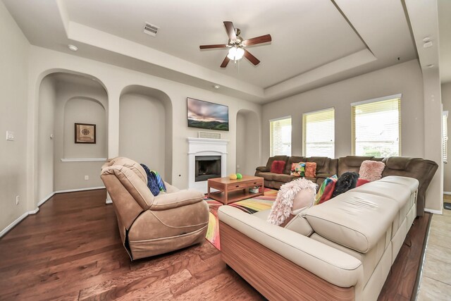 13906 Mowbray Ct, Richmond, TX 77407 - living room featuring a raised ceiling, ceiling fan, baseboards, a fireplace, and wood finished floors