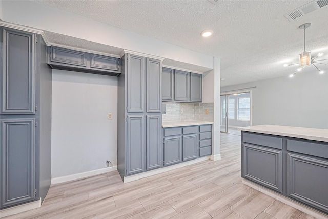 2115 Streamcrest Ln, Sugar Land, TX 77479 - kitchen with a textured ceiling, light countertops, baseboards, light wood-style flooring, and hanging light fixtures