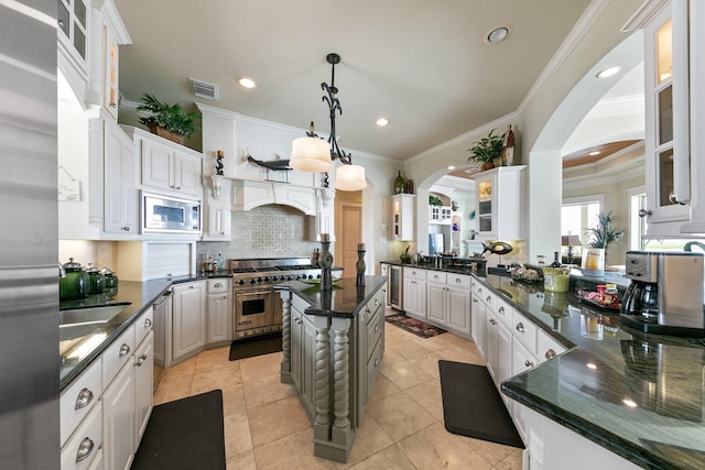4115 Sand Hill Ct, Galveston, TX 77554 - kitchen featuring appliances with stainless steel finishes, arched walkways, decorative backsplash, crown molding, and glass insert cabinets